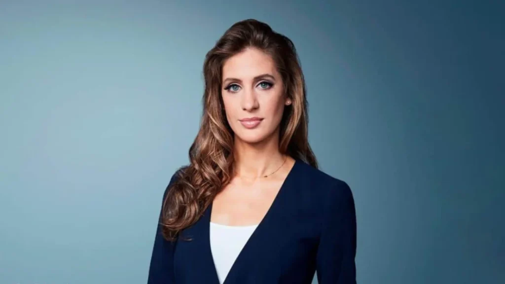 Professional CNN headshot of a brunette woman with blue eyes wearing a navy blazer against a blue-gray background.